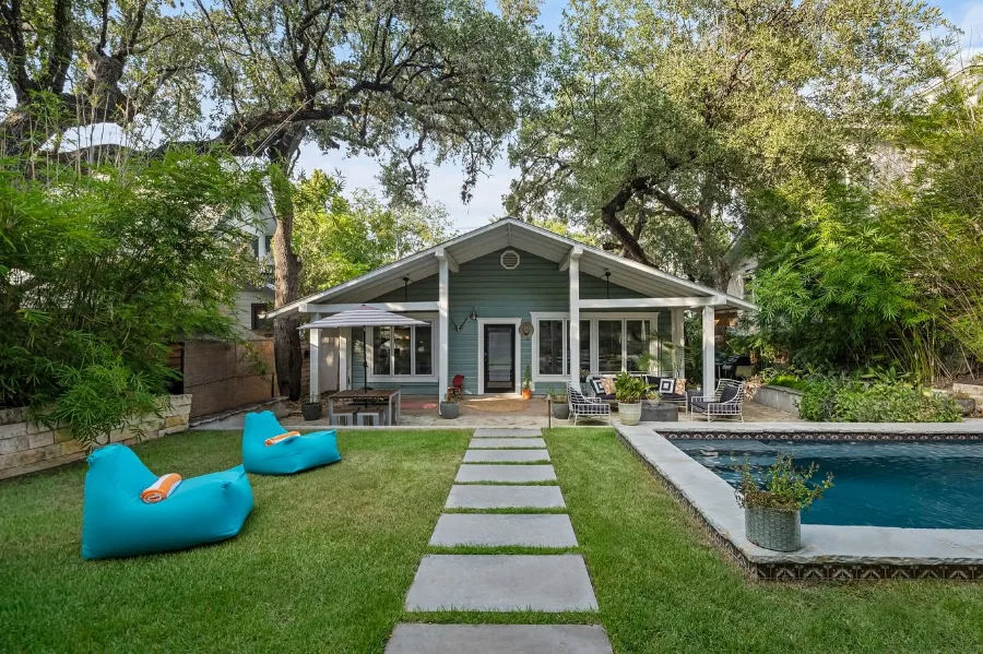Green bungalow with a covered patio, stepping-stone path, mature trees and a pool, from Leila Showery’s existing website image collection.